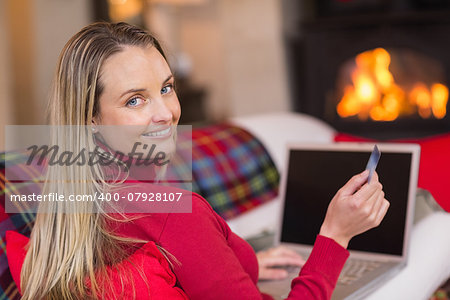 Smiling blonde shopping online with laptop at christmas at home in the living room