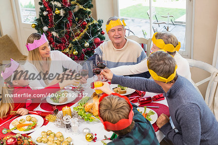 Family in party hat toasting at christmas dinner at home in the living room