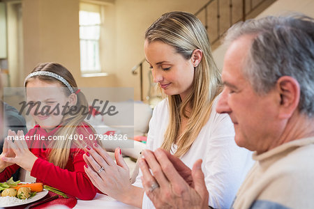 Extended family saying grace before christmas dinner at home in the dining room