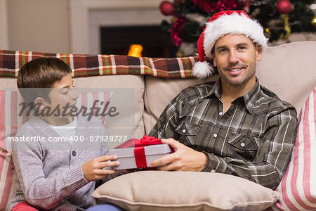 Son giving father a christmas gift on the couch at home in the living room