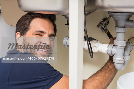 Happy plumber fixing under the sink in the kitchen