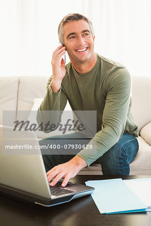 Happy man on the phone using laptop at home in the living room