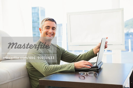 Smiling man using laptop with glasses on the table at home in the living room