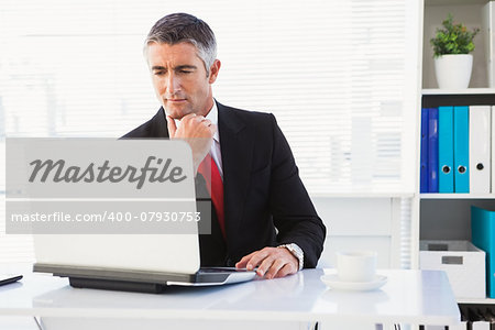 Focused businessman in suit using his laptop in his office