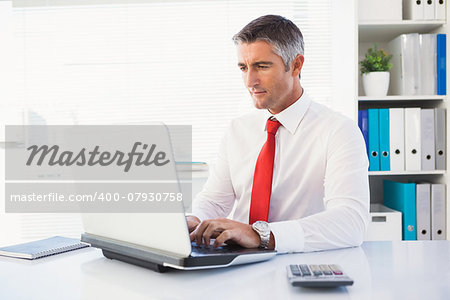 Cheerful businessman typing on laptop in his office