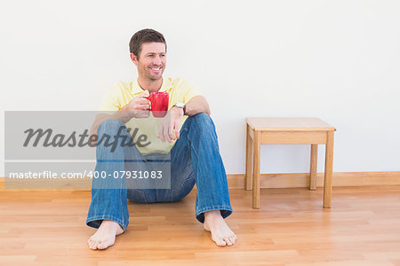 Casual man sitting on floor holding a mug at home in the living room