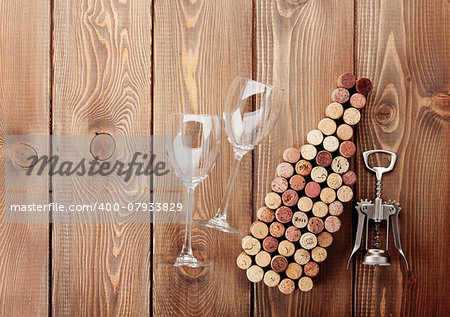 Wine bottle shaped corks, glasses and corkscrew over rustic wooden table background. View from above with copy space