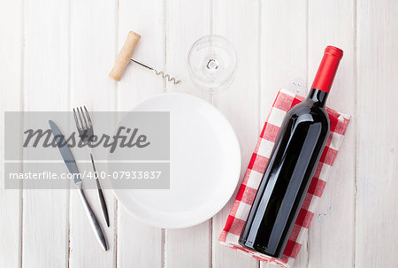 Table setting with empty plate, wine glass and red wine bottle. View from above over rustic wooden table background