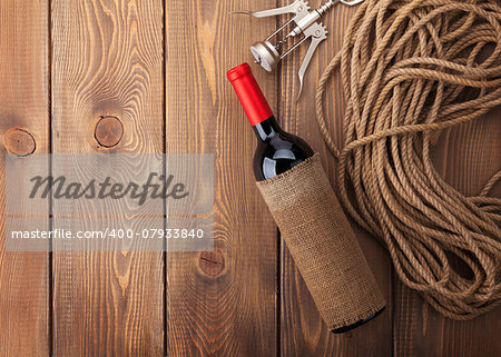 Red wine bottle and corkscrew over rustic wooden table background with copy space