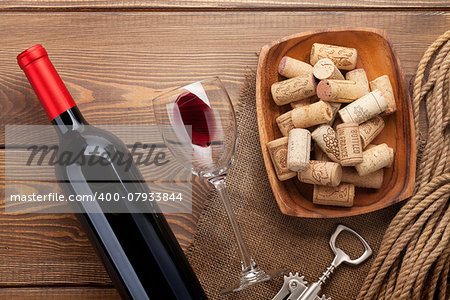 Red wine bottle, glass of wine, bowl with corks and corkscrew. View from above over rustic wooden table background