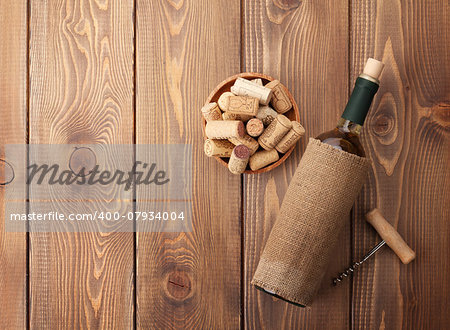 White wine bottle, bowl with corks and corkscrew. View from above over rustic wooden table background