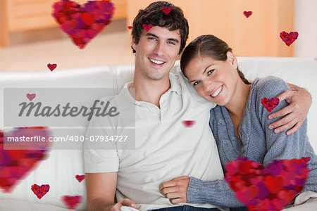 Happy couple enjoying their time together on the couch against hearts