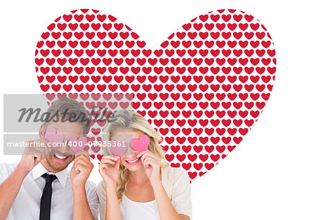 Attractive young couple holding pink hearts over eyes against valentines day pattern