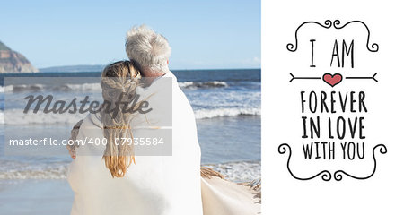 Couple wrapped up in blanket on the beach looking out to sea against valentines message