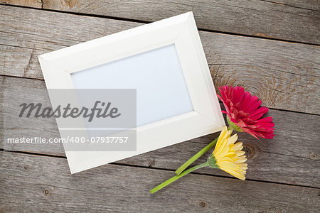 Two colorful gerbera flowers and photo frame on wooden table