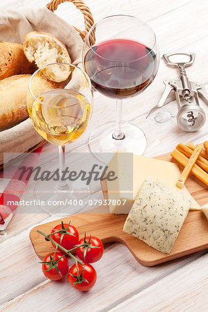 White and red wine glasses, cheese and bread on white wooden table background