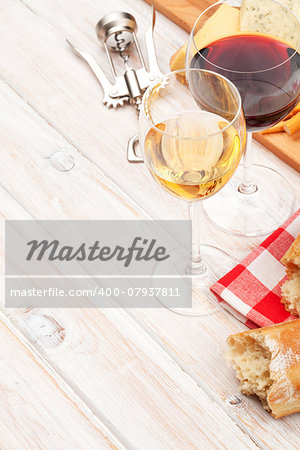 White and red wine glasses, cheese and bread on white wooden table background with copy space