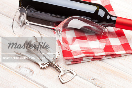 Red wine bottle, glass and corkscrew on white wooden table background