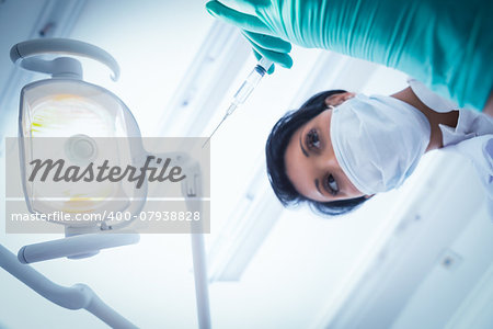 Low angle view of female dentist in surgical mask holding injection