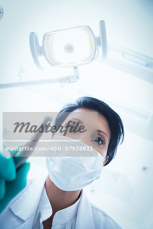 Low angle view of female dentist in surgical mask holding dental drill