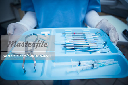 Close up mid section of female dentist in blue scrubs holding tray of tools