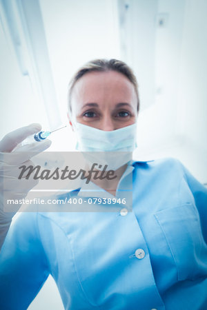 Low angle portrait of female dentist in surgical mask holding injection