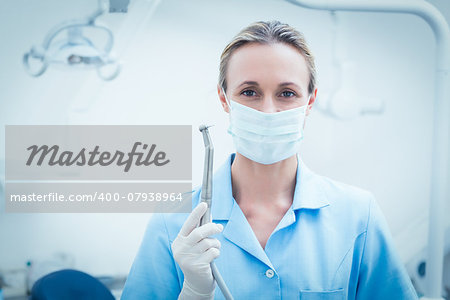 Portrait of female dentist in surgical mask holding dental tool