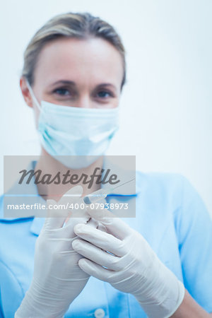 Portrait of young female dentist in surgical mask holding injection