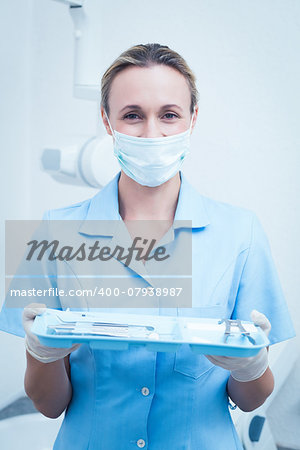 Portrait of female dentist in surgical mask holding tray of tools