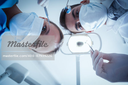 Low angle view of dentists in surgical masks holding dental tools