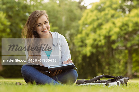Smiling student sitting and holding book in park at school