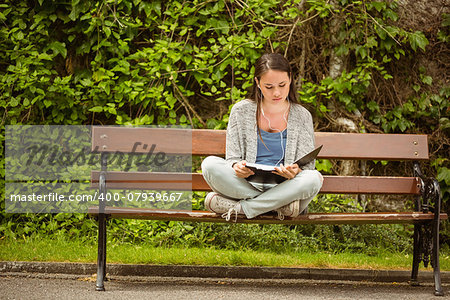 Student sitting on bench listening music with mobile phone and revising in park at school