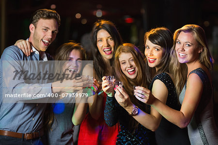 Happy friends drinking shots smiling at camera at the nightclub