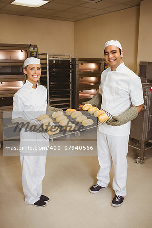 Team of bakers holding rack of rolls in a commercial kitchen