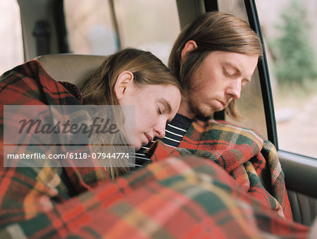 A couple taking a nap in their car, covered by a blanket. A couple taking a nap in their car, covered by a blanket.