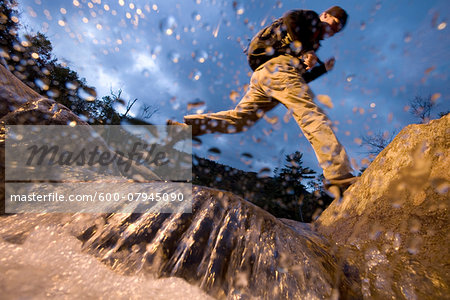 Low angle view of man jumping over a stream while hiking in New Hampshire, USA Low angle view of man jumping over a stream while hiking in New Hampshire, USA
