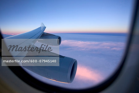 An aircraft wing and engines as seen from the window of a jet while flying above the clouds at sunset. An aircraft wing and engines as seen from the window of a jet while flying above the clouds at sunset.