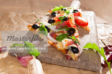 Pizza piece with colorful delicious vivid toppings on wooden cutting board with garlic, chili pepper and vine cork. Italian culinary eating.