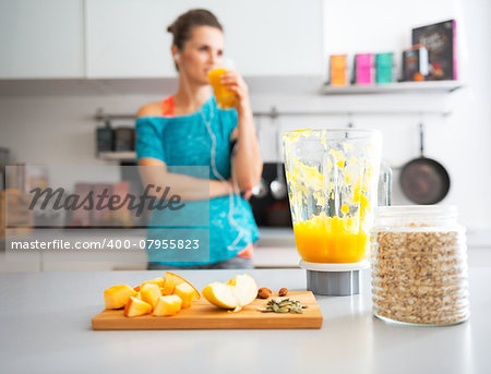 Close-up on pumpkin smoothie and ingredients on table and fitness young woman in background