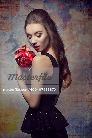 Romantic, young, beautiful, bright, elegant girl in black dress is holding valentines present. Her makeup is perfect.