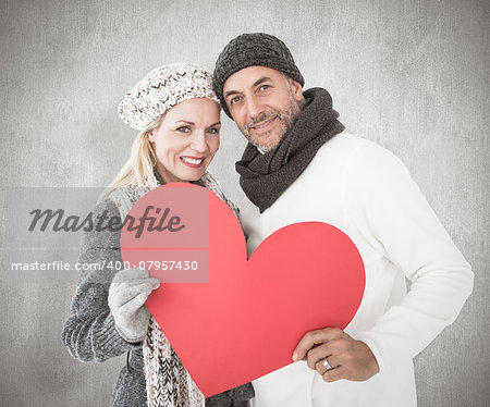 Smiling couple in winter fashion posing with heart shape against weathered surface