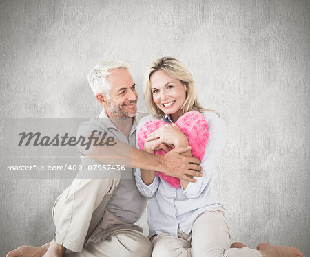 Happy couple sitting and holding heart pillow against weathered surface