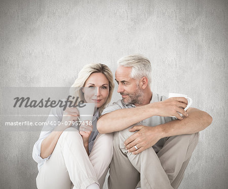 Happy couple sitting holding mugs against weathered surface