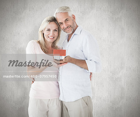 Happy couple holding miniature model house against weathered surface