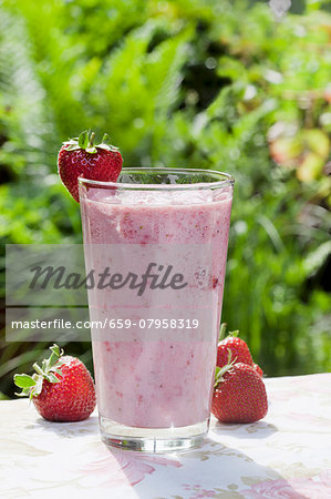 A strawberry smoothie and strawberries on a garden table