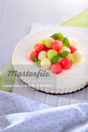 A cream cheesecake decorated with colourful melon balls and peppermint leaves