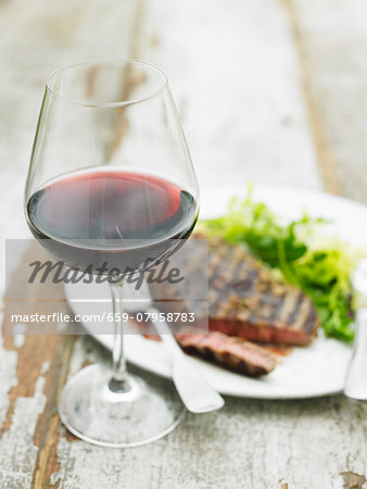 A glass of red wine in front of a grilled beef steak with salad A glass of red wine in front of a grilled beef steak with salad