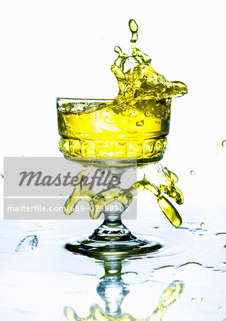 A yellow drink splashing from a glass