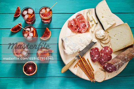 An Italian appetiser platter next to glasses of aperitifs garnished with slices of blood orange