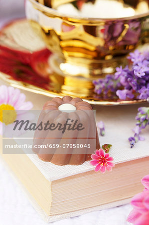 A chocolate praline with white decorations on a book in front of a brass bowl